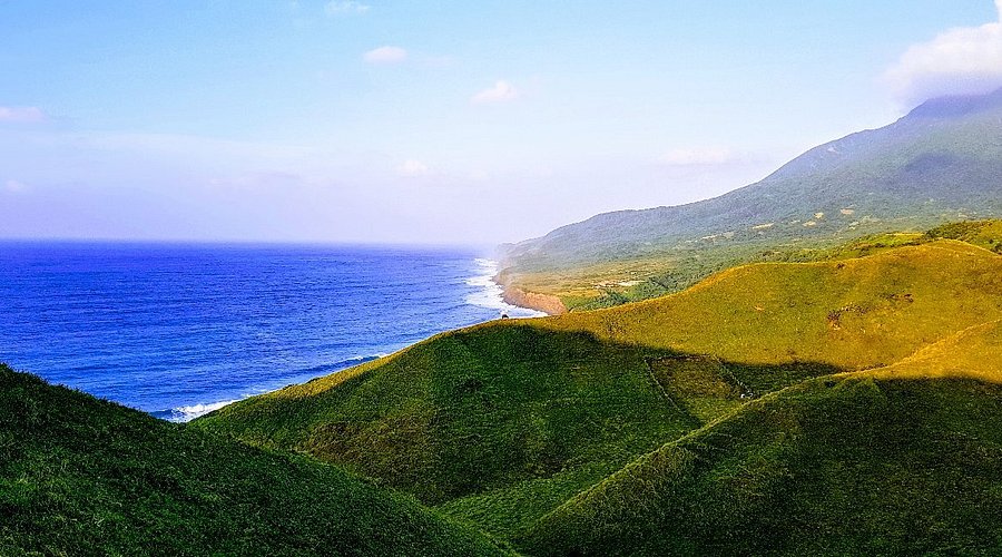Rolling green hills of Batan Island meeting the Pacific coastline
